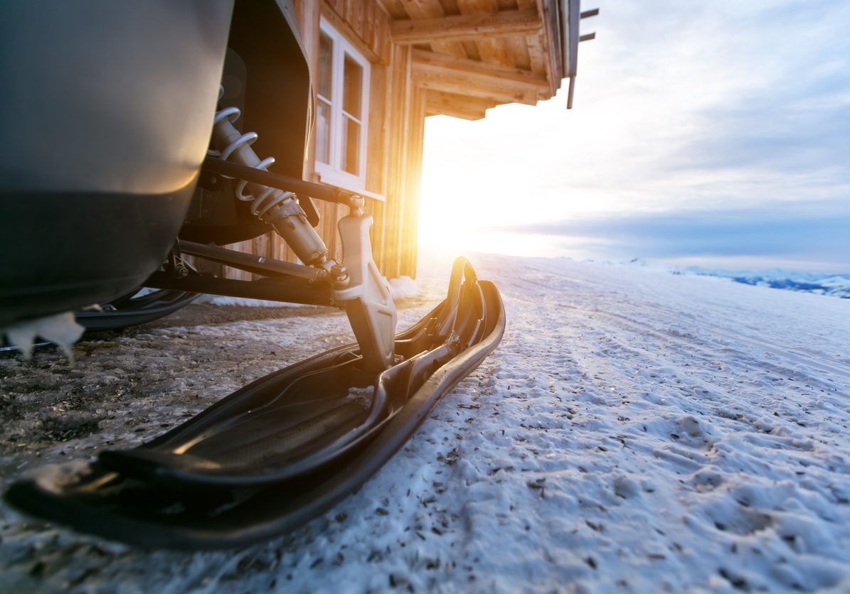 Closeup of snowmobile parking next to log cabin in mountains. Winter outdoor snow activities